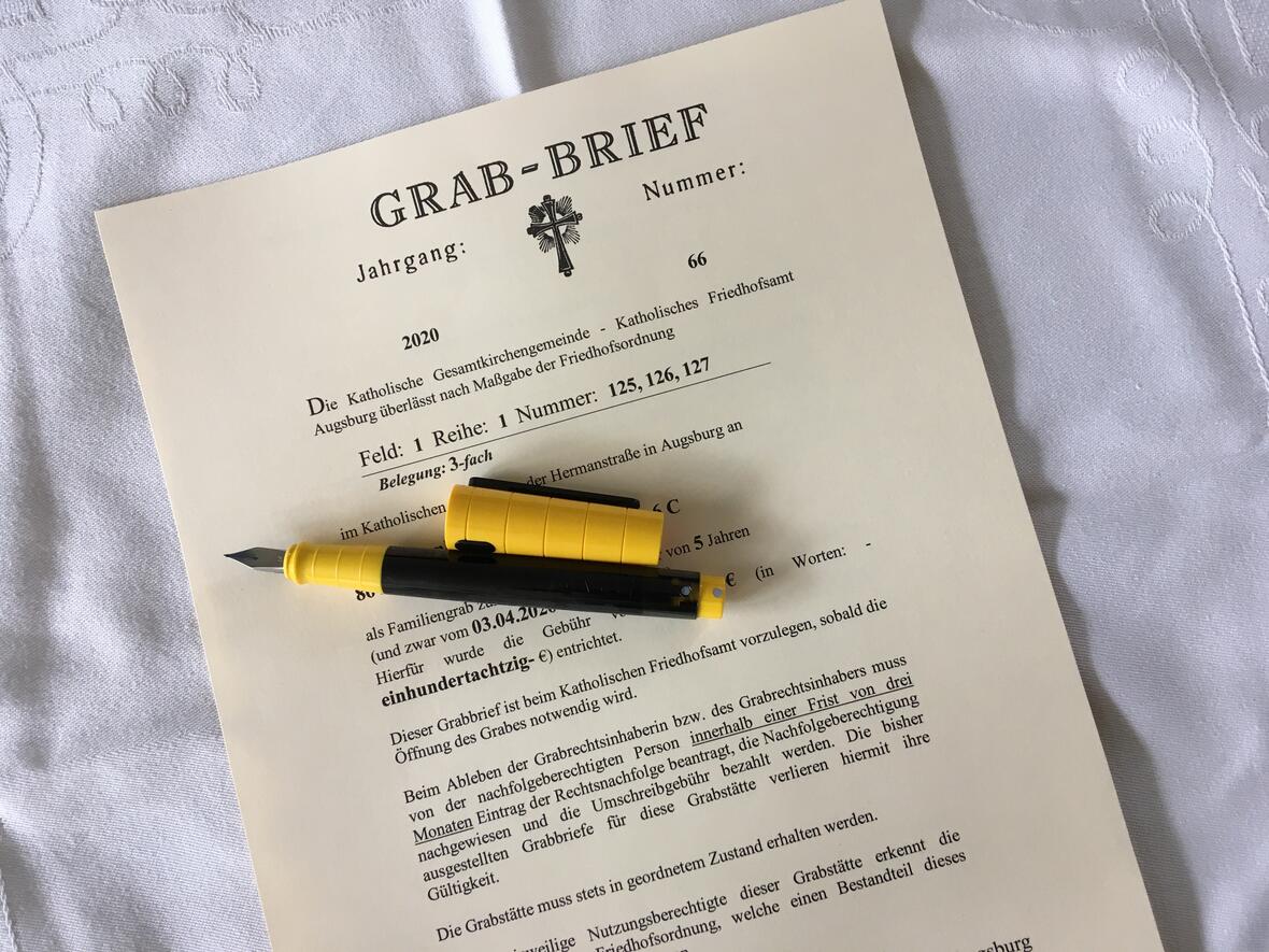 Auf einem Grabbrief liegt ein gelber Füllfederhalter